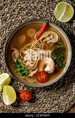 Asiatische würzige Nudeln Suppe mit Shiitake-Champignons und Garnelen, Zutaten oben auf Strohfellernte als Hintergrund. Flaches Layout, Platz. Asiatisches Dinn Stockfoto
