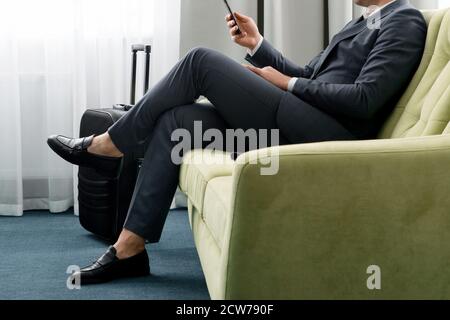 Ein fröhlicher Geschäftsmann, der mit dem Koffer im Hotelzimmer telefoniert Auf Geschäftsreise Stockfoto