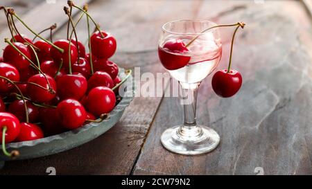 Kirsch oder Kirschwasser - ein starkes alkoholisches Kirschgetränk Ein Glas und frische Kirsche auf einem alten dunklen Holz Tabelle Stockfoto