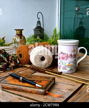 Konzept der Entspannung mit einem Leder gebunden Journal, verschiedene Strick-Accessoires, floral china Tee Tasse in einem Stillleben Komposition in einem rustikalen Garten Stockfoto