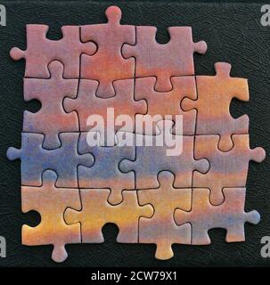 Ein Quadrat aus bunten Puzzleteilen isoliert auf einem schwarzen strukturierten Hintergrund. Stockfoto