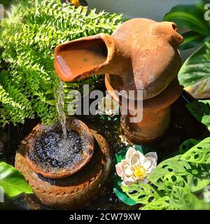 Luftaufnahme eines Terrakotta-Wasserzeichens, mit Wasser, das aus einer geneigten Urne kaskadiert. Der Brunnen ist von üppiger, grüner tropischer Vegetation umgeben. Stockfoto