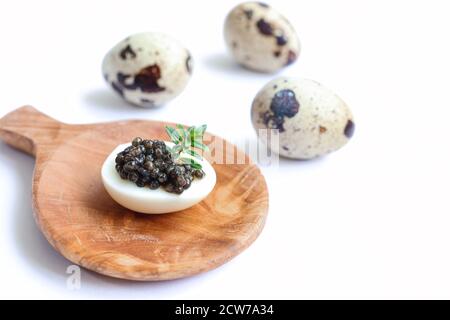 Köstlicher schwarzer Stör-Kaviar auf einem Wachtelei mit Rosmarin Auf der Holzplatte und frische Wachteleier isoliert auf Der weiße Hintergrund Stockfoto