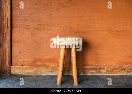 Handgefertigter Stuhl aus Holz mit Korbstrohkissen auf dem Hintergrund der roten Terrakotta-Wand mit dekorativem Gips. Marokkanische rustikale Einrichtung und Möbeldesign. Stockfoto