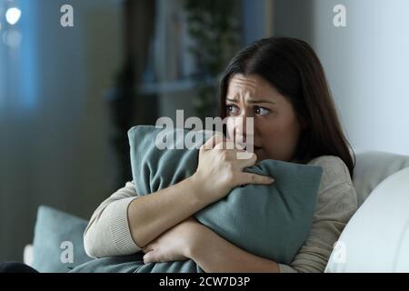 Verängstigte Frau umarmt Kissen in der Nacht auf einem sitzen Couch im Wohnzimmer zu Hause Stockfoto