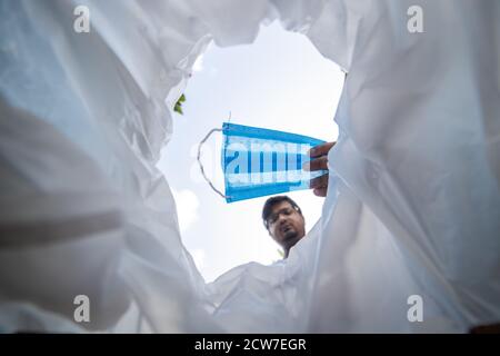 Low-Angle-Ansicht des Menschen werfen gebrauchte Gesichtsmaske in Mülleimer Stockfoto