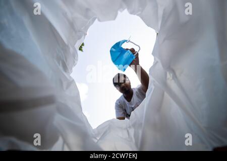 Low-Angle-Ansicht des Menschen werfen gebrauchte Gesichtsmaske in Mülleimer Stockfoto