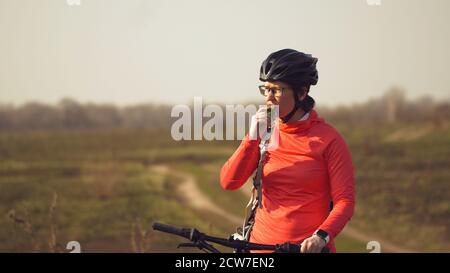 Athletische kaukasische Frau isst Protein-Bar-Fahrt auf dem Mountainbike auf der Natur. Junge sportliche Frau Athlet in Helm ruhen während Beißen Ernährungsriegel Stockfoto