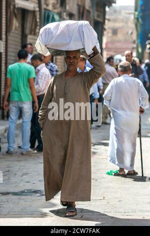 Ein ägyptischer Mann, der eine Ladung Waren auf seinem Kopf trägt, geht durch den Khan el Khal'ili Basar in Kairo in Ägypten. Stockfoto