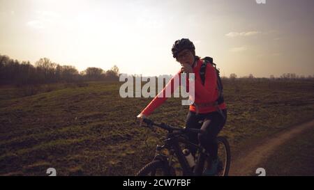 Athletische kaukasische Frau isst Protein-Bar-Fahrt auf dem Mountainbike auf der Natur. Junge sportliche Frau Athlet in Helm ruhen während Beißen Ernährungsriegel Stockfoto