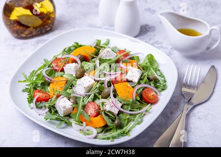 Warmer Salat mit Kürbis, Feta-Käse, Tomaten, Kapern, Rucola und roten Zwiebeln. Nahaufnahme. Stockfoto