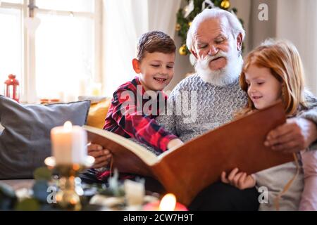 Kleine Kinder mit älteren Großvater drinnen zu Hause zu Weihnachten, Blick auf Fotos. Stockfoto