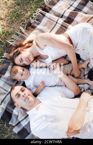 Mama, Papa und kleiner Sohn liegen auf der Decke im Sommerpark. Das Konzept des Sommerurlaubs. Mutter, Vater, Baby Tag. Familie verbringt Zeit Stockfoto