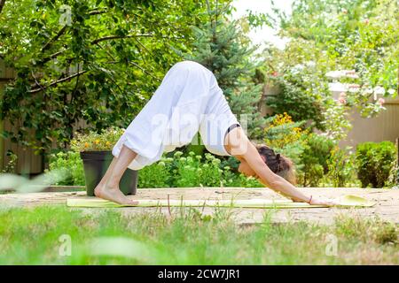 Junge Frau praktiziert Yoga im Garten - Parvatasana. Stockfoto