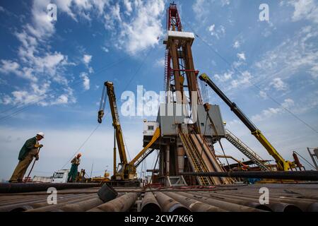 Zhaik-Munai Öllagerstätte, Kasachstan. Ölbohranlage, Bohrrohre, Krane, Ausrüstung und Ölarbeiter.Blauer Himmel mit Wolken. Stockfoto