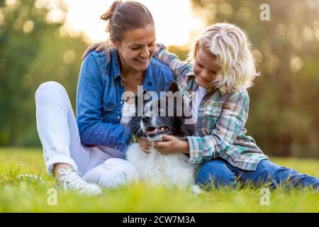 Glückliche Mutter und Sohn im Freien streicheln ihren Hund Stockfoto