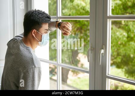 Junger asiatischer Mann, der sich gegen das Fenster lehnte und auf Bäume draußen schaute