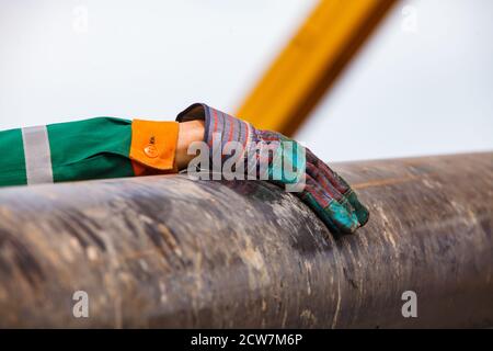 Arbeitshandschuh und grün und orange Arbeitskleidung von Ölarbeiter mit verrosteten Bohrrohr. Öllagerstätte Zhaik-Munai, Kasachstan. Stockfoto