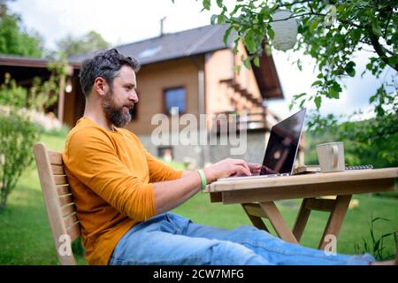 Seitenansicht des Mannes mit Laptop, der im Garten arbeitet, Home Office-Konzept. Stockfoto