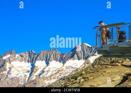 Eggishorn, Kanton Wallis, Schweiz - 6. August 2020: Touristen Wanderer auf Aussichtsplattform Blick auf Aletschgletscher auf Eggishorn Gipfel mit gedeckelten Stockfoto