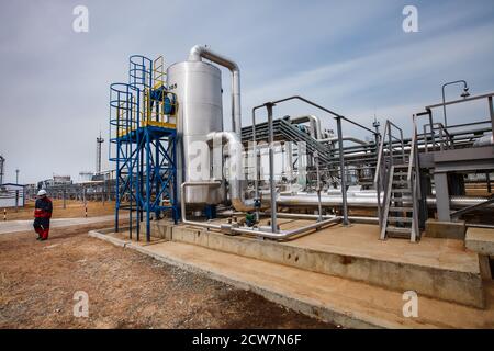 Raffinerieanlagen, Rohre, Rohrleitungen und Arbeiter oder Ingenieur. Ölraffinerie und Gasverarbeitungsanlage. Raffineriearbeiter in roter Arbeitskleidung links. Stockfoto