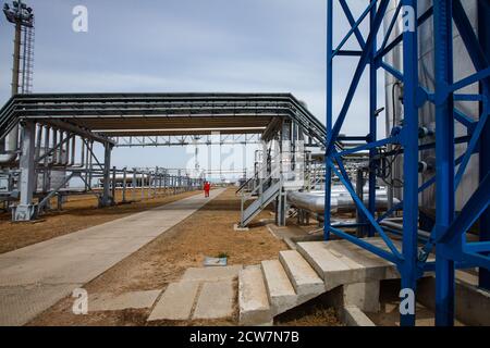 Ölraffinerie und Gasverarbeitungsanlage. Pipelines und Mast am grauen Himmel. Raffineriearbeiter im Hintergrund. Zhaik-Munai Öllagerstätte, Kasachstan. Stockfoto