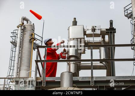 Zhaik-Munai Öllagerstätte, Kasachstan. Ölraffinerie und Gasverarbeitungsanlage. Ölarbeiter (Ingenieur) in roten Overalls und weißem Harthut bei der Arbeit. Stockfoto