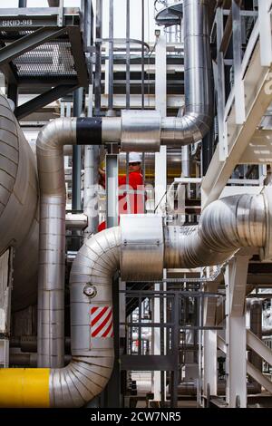 Ölraffinerie und Gasverarbeitungsanlage. Ölingenieur in rot insgesamt und Helm auf der Metalltreppe an Rohren bkgd. Zhaik-Munai Öllagerstätte, Kasachstan. Stockfoto