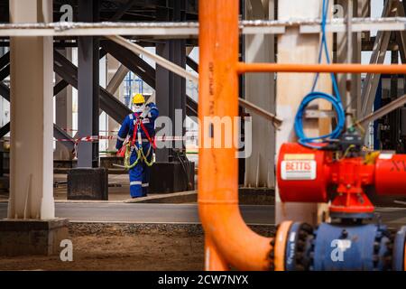 Zhaik-Munai Öllagerstätte, Kasachstan. Ölraffinerie und Gasverarbeitungsanlage. Industriekletterer in blauer Arbeitskleidung und gelbem Helm. Konzentrieren Sie sich auf den Menschen. Stockfoto