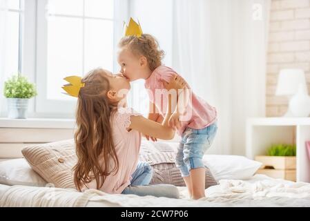 Zwei nette Kinder Baby Mädchen spielen und Spaß im Kinderzimmer. Liebevolle Schwestern mit Kronen auf dem Bett. Stockfoto