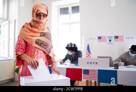 Islamische Wählerin, die ihre Stimme in die Wahlurne stellt, Wahlen in den usa und Coronavirus. Stockfoto