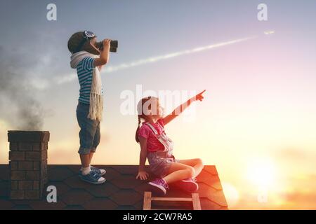 Zwei kleine Kinder spielen auf dem Dach des Hauses und schauen in den Himmel und träumen davon, Pilot zu werden. Stockfoto