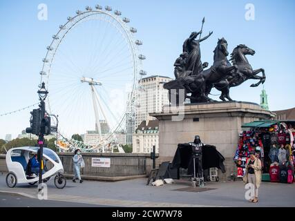 Ein Straßenkünstler, der als Star Wars-Bösewicht gekleidet ist, Darth Vader tritt auf der Westminster Bridge in London zu spärlichen Menschenmassen auf, nachdem in England eine Reihe neuer Beschränkungen gegen den Anstieg von Coronavirus-Fällen in Kraft traten. Stockfoto