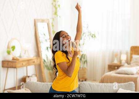 Fröhliche schwarze Frau mit Haarbürste als mic singen ihren Favoriten Gesang und Tanz zu Hause Stockfoto