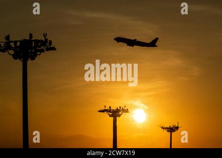 Passagierflugzeug ist Start während eines schönen Sonnenaufgangs. Lampenturm von Scheinwerfern auf den Säulen am Flughafen. Stockfoto