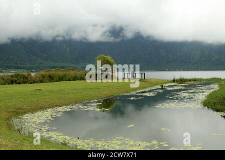 Ort des Gebets und der Kraft. Bratan See im Nebel. Traditionelle balinesische Ritualangebote in Strohkörben für hinduistische Geister und Götter mit Blumen und aromatischen Stäbchen Stockfoto