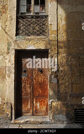 Sonnenlicht wirft ein warmes Licht auf die rostende Tür und Steinfassade eines alten Gebäudes in Valletta, Malta. Stockfoto