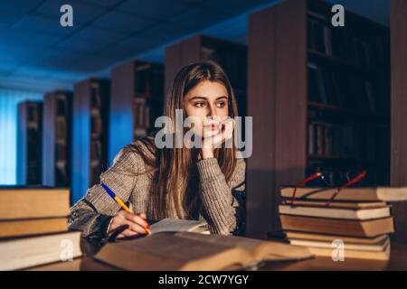 Junge Studentin in Brille Vorbereitung auf die Prüfung. Mädchen am Abend sitzt an einem Tisch in der Bibliothek mit einem Stapel von Büchern. Stockfoto