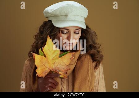 Hallo Herbst. Verträumte trendige Frau im Schal mit Lederhandschuhen und gelben Herbst Ahornblätter auf beigem Hintergrund. Stockfoto