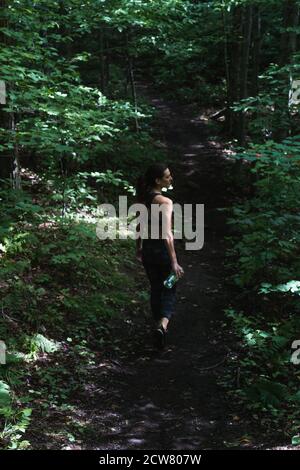 Eine junge Frau, die durch einen Pfad in den Adirondacks wandert und eine Wasserflasche hält Stockfoto