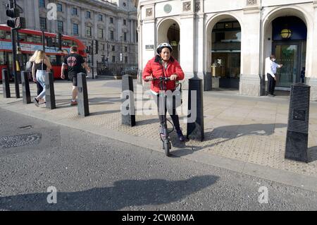 London, England, Großbritannien. Frau auf dem Parliament Square, die einen E-Scooter vom Straßenbelag über eine Fußgängerüberfahrt fährt Stockfoto