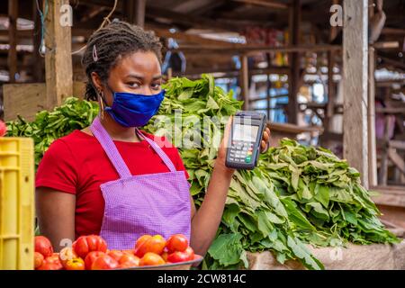 Porträt einer afrikanischen Marktfrau mit Gesichtsmaske Halten eines POS-Geräts Stockfoto