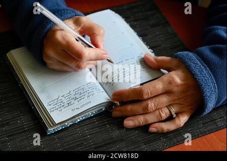 Nahaufnahme einer älteren Frau, die einen Eintrag in ihr Tagebuch schreibt. Stockfoto