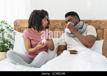 Kranker afroamerikanischer Mann in Schal gewickelt im Bett sitzend Stockfoto