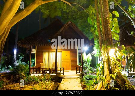 Holzbungalow im Wald. Haus in der Nacht im Dschungel. Hohe grüne tropische Bäume im Vordergrund, im Hintergrund ein Sternenhimmel. Stockfoto