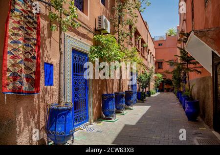 Typische schmale Straße in Marrakesch mit Teppich, leuchtend blauen Keramik Blumentöpfen, blau bemalten Türen, rot weiß getünchten Wand. Stockfoto