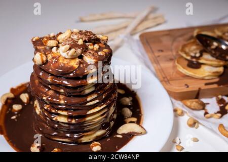 Schokoladen-Pfannkuchen mit Bananen, Nüssen und Schokoladensauce. Die Tonung. Holzbrett mit Pfannkuchen auf dem Hintergrund. Stockfoto