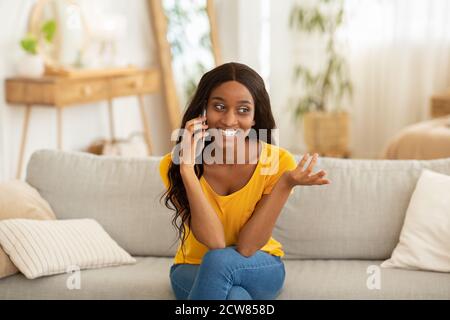 Positive junge schwarze Dame, die am Handy chattet und lächelt Sofa zu Hause Stockfoto