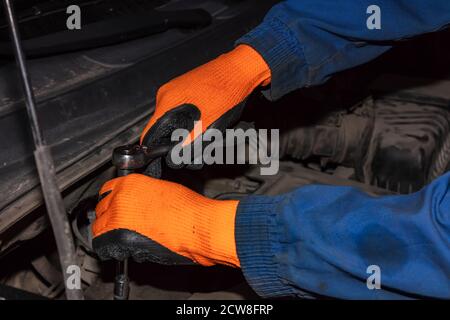Handschuhen von Mechaniker halten Schlüssel oder Schraubenschlüssel arbeiten am Motor. Mechaniker trägt orange Handschuhe und blaues Outfit mit Öl bedeckt. Stockfoto