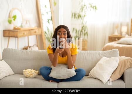 Unterhaltung am Wochenende. Schockiert afroamerikanische Frau mit TV-Controller genießen interessante Film drinnen Stockfoto